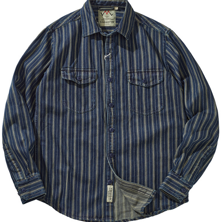 A striped denim shirt with blue, white, and gold vertical stripes, two chest pockets with button flaps, and a collar. The relaxed-fit button-down is laid flat with the bottom slightly folded to reveal the inner tag.
