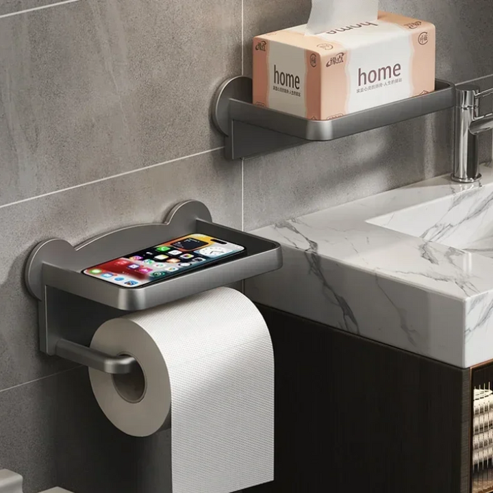 A moisture-resistant toilet paper holder with a built-in tray for your smartphone is mounted on the bathroom wall; above, a multi-functional shelf holds a tissue box beside a sink with a marble countertop.