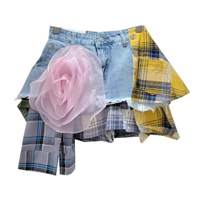 A patchwork skirt made of blue denim and multicolored plaid fabric panels, featuring a large, sheer pink flower decoration on the front left side—perfect for eclectic fashion lovers.