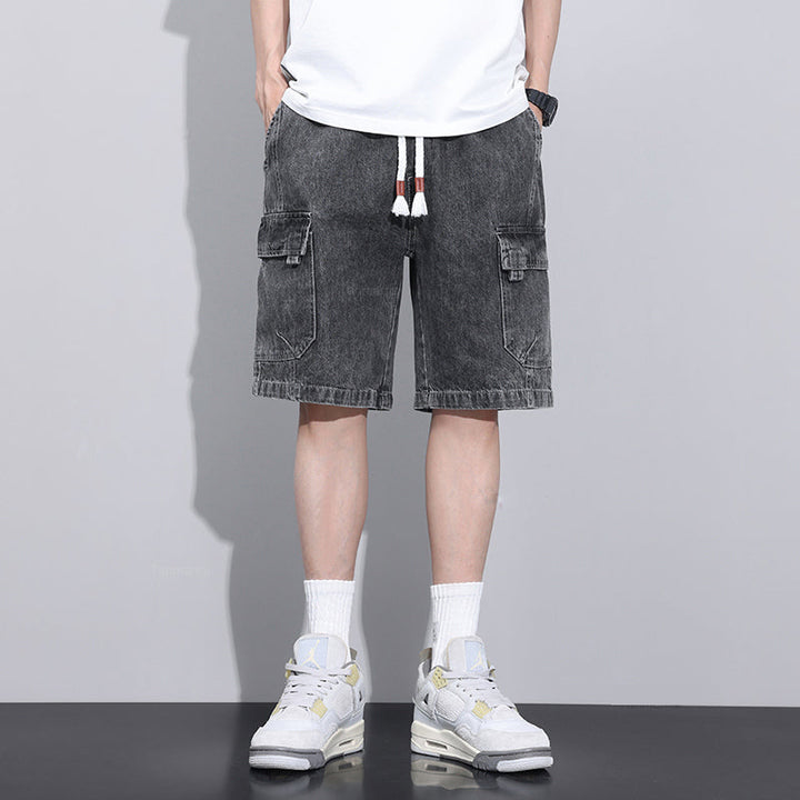 A person wearing a white t-shirt, mens denim shorts with an elastic waist and drawstrings, white crew socks, and white sneakers stands against a plain gray background. Their hands are in their pockets, and their face is not visible.
