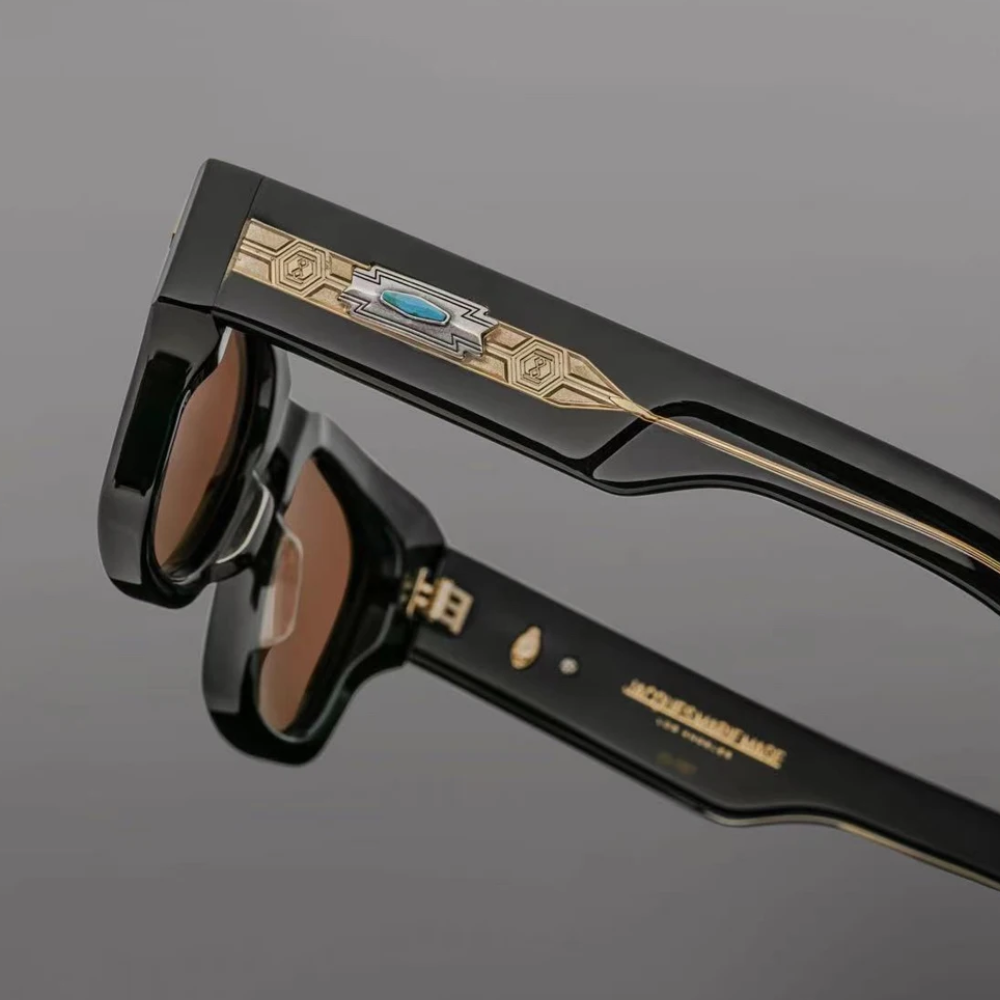 Close-up of retro sunglasses with black frames, gold geometric detailing, and a turquoise accent on the arms, set against a plain gray background. Features UV400 protection for stylish eye safety.