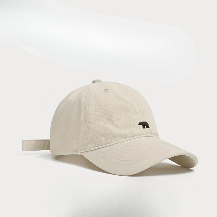 A light beige baseball cap crafted from premium cotton, featuring a curved brim and a small black bear logo on the front, displayed against a plain white background.