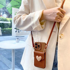 A person in a cream blazer holds a brown purse with a chic phone case and beige heart design, standing indoors near a window with greenery and outdoor seating visible outside.