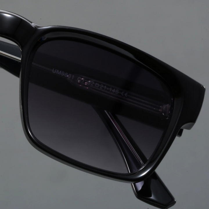 Close-up of the right side of black rectangular sunglasses with durable frames and dark tinted lenses, featuring visible frame details and a modern design, set against a plain gray background.