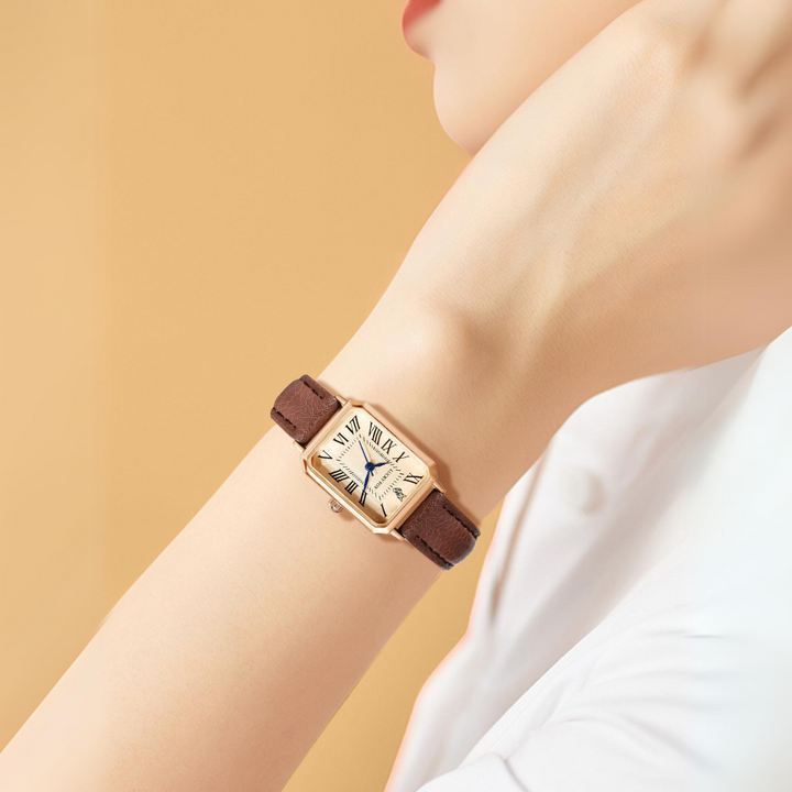 A person wears a rectangular face watch with a genuine leather strap. The gold watch features Roman numerals and blue hands. Against a soft beige background, the individual is dressed in elegant white attire.