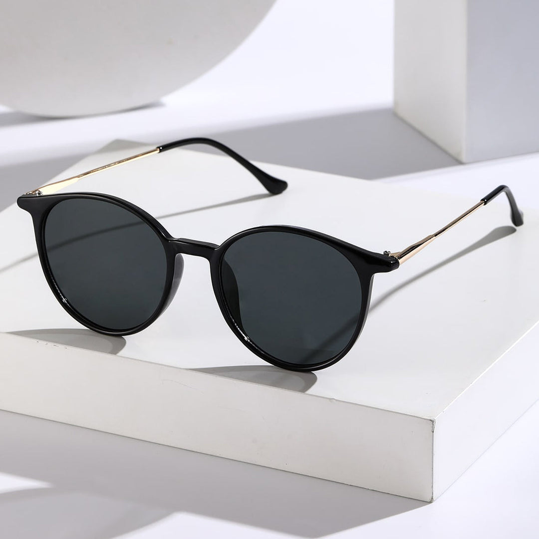 A pair of black round sunglasses with dark tinted, anti-glare lenses and thin gold arms, offering reliable UV protection, displayed on a white geometric surface with soft shadows.
