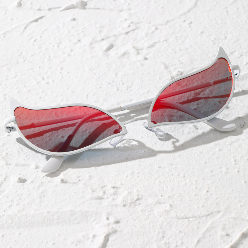 Cat-eye sunglasses with a lightweight frame and red-tinted, polarized lenses rest on a textured white surface, with shadows and sunlight reflecting off the glasses.