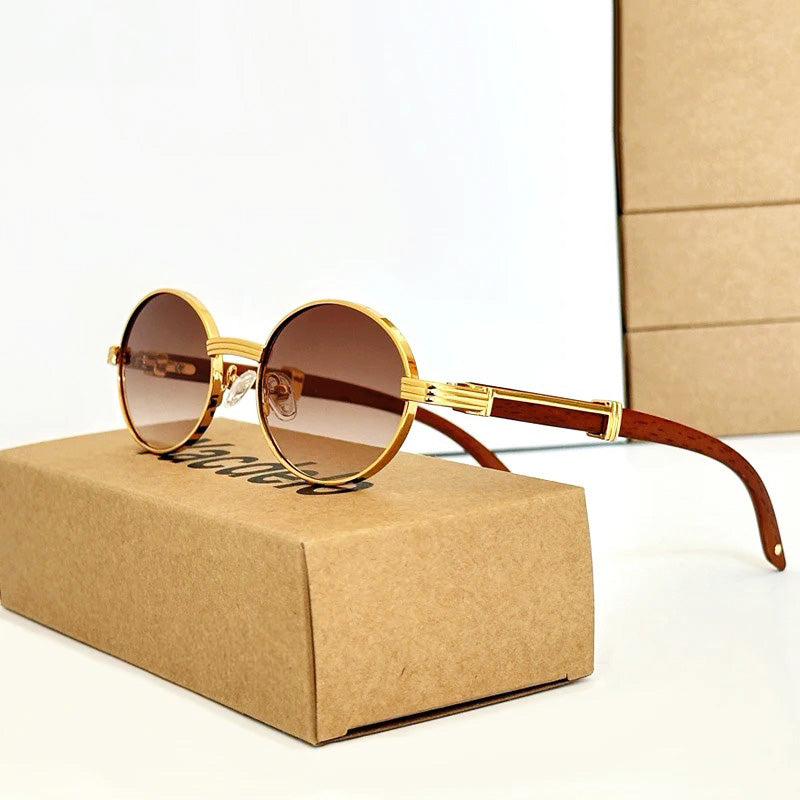 Vintage round sunglasses with gold frames and brown gradient UV400 protection lenses rest on a closed cardboard box; another box stands vertically in the background.