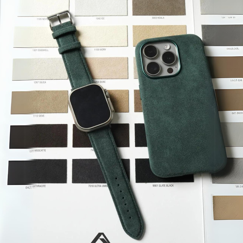 A green Alcantara suede smartwatch band with a stainless steel buckle and a matching phone case rest atop a neutral color palette chart featuring various beige, brown, and black swatches.