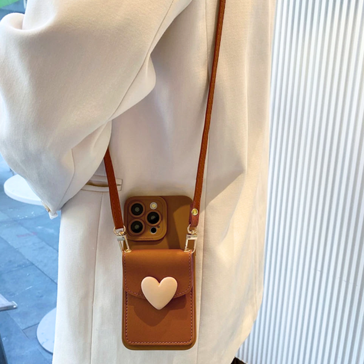 A person wearing a cream-colored coat carries a small brown phone pouch with a heart-shaped clasp and crossbody strap, partially open to reveal a smartphone inside.