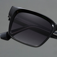 Close-up of black rectangular sunglasses with modern design and dark tinted lenses, crafted with durable frames and UV400 protection, shown against a plain gray background.