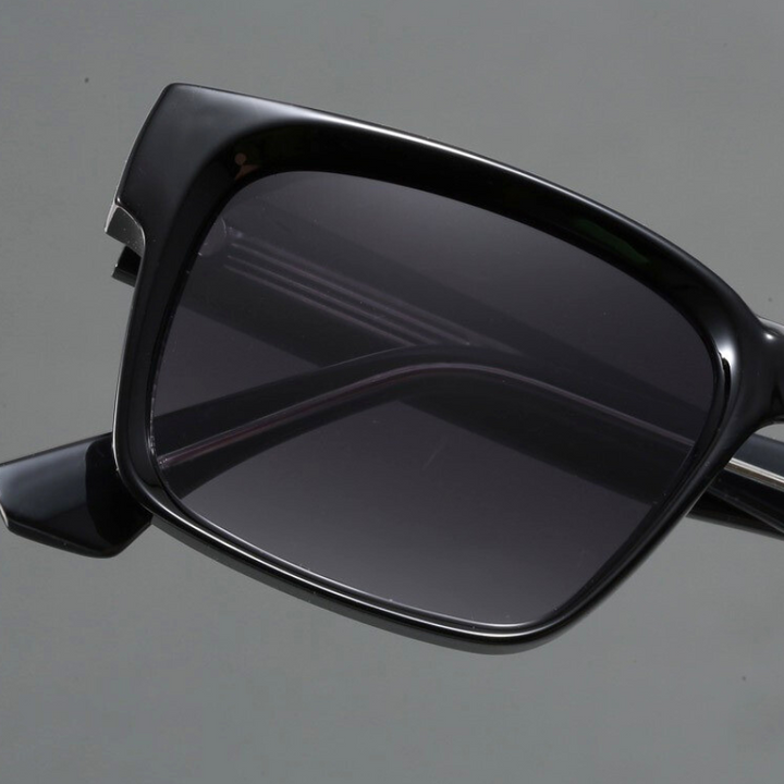 Close-up of black rectangular sunglasses with modern design and dark tinted lenses, crafted with durable frames and UV400 protection, shown against a plain gray background.