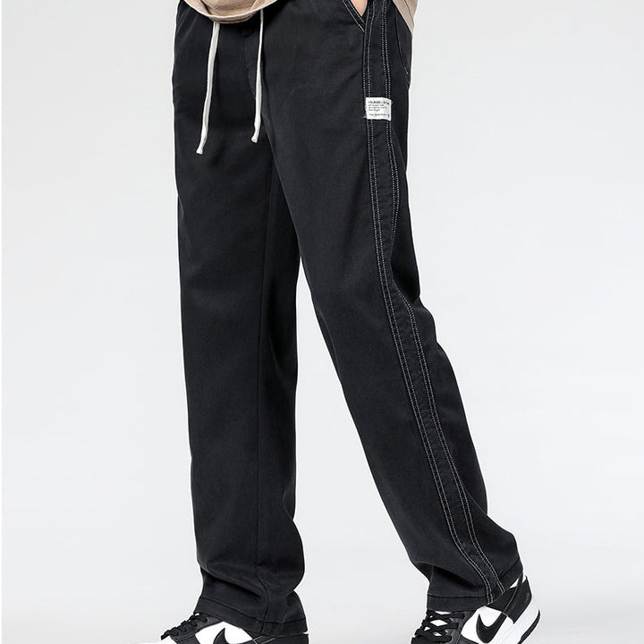 Person wearing summer loose men jeans in black with white contrast stitching and drawstrings, paired with black and white Nike sneakers, standing against a plain light background.