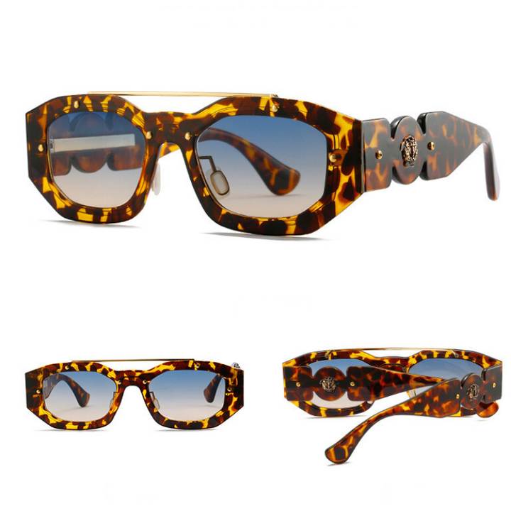 Tortoiseshell sunglasses with thick, geometric frames and wide arms, featuring a decorative round emblem on the temples. The gradient lenses offer UV400 protection, transitioning from dark at the top to lighter at the bottom.