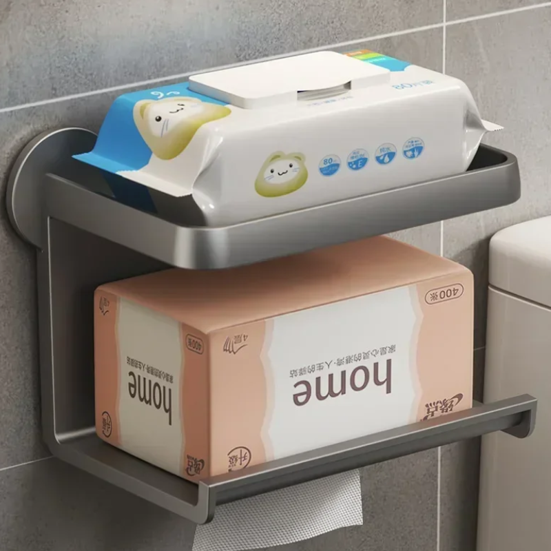 A moisture-resistant, wall-mounted metal shelf in a bathroom holds wet wipes on the top shelf and tissues on the bottom, mounted above a toilet against gray tiled walls.