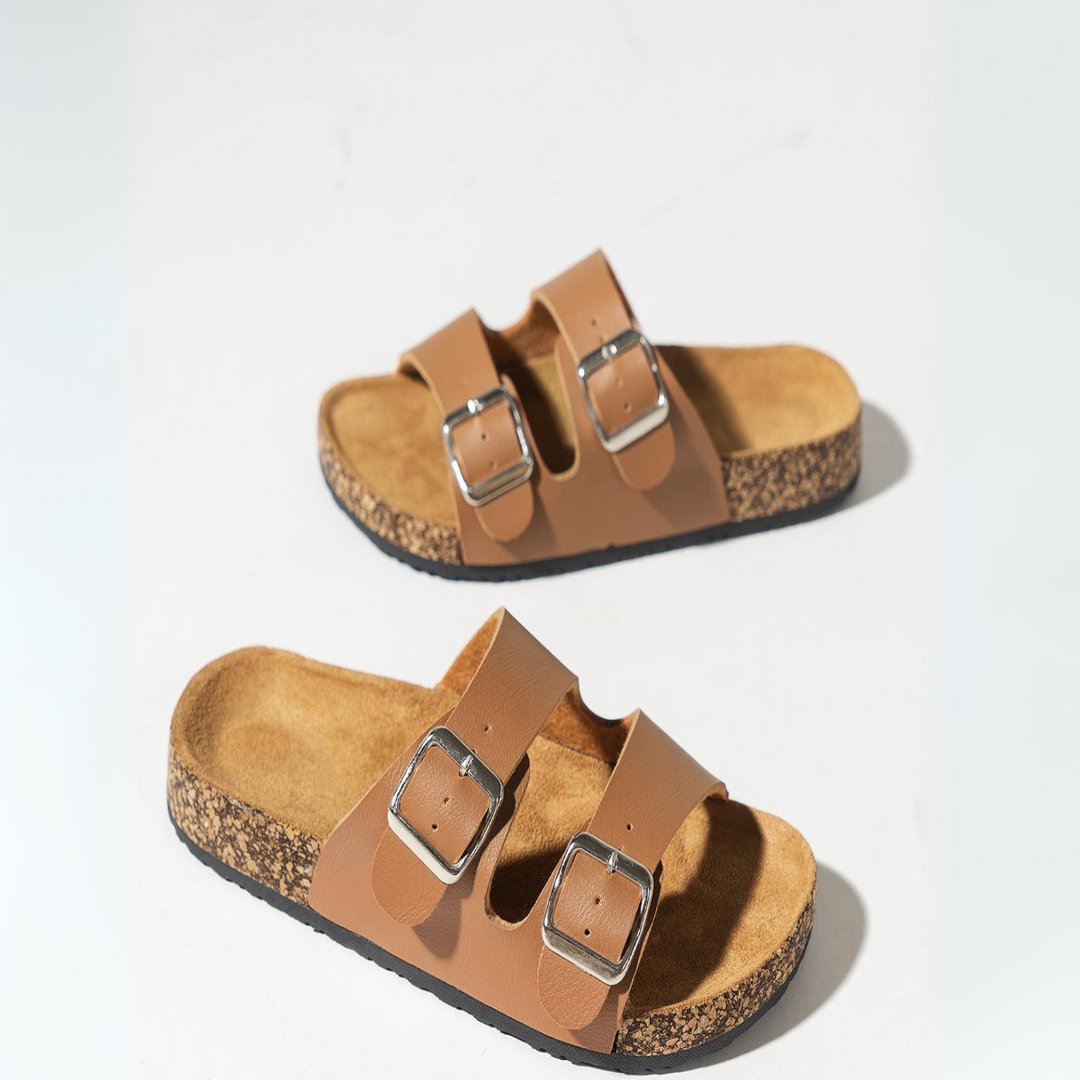 A pair of double-buckle sandals with premium leather straps and silver buckles, featuring ergonomic cork footbeds, placed on a white surface.