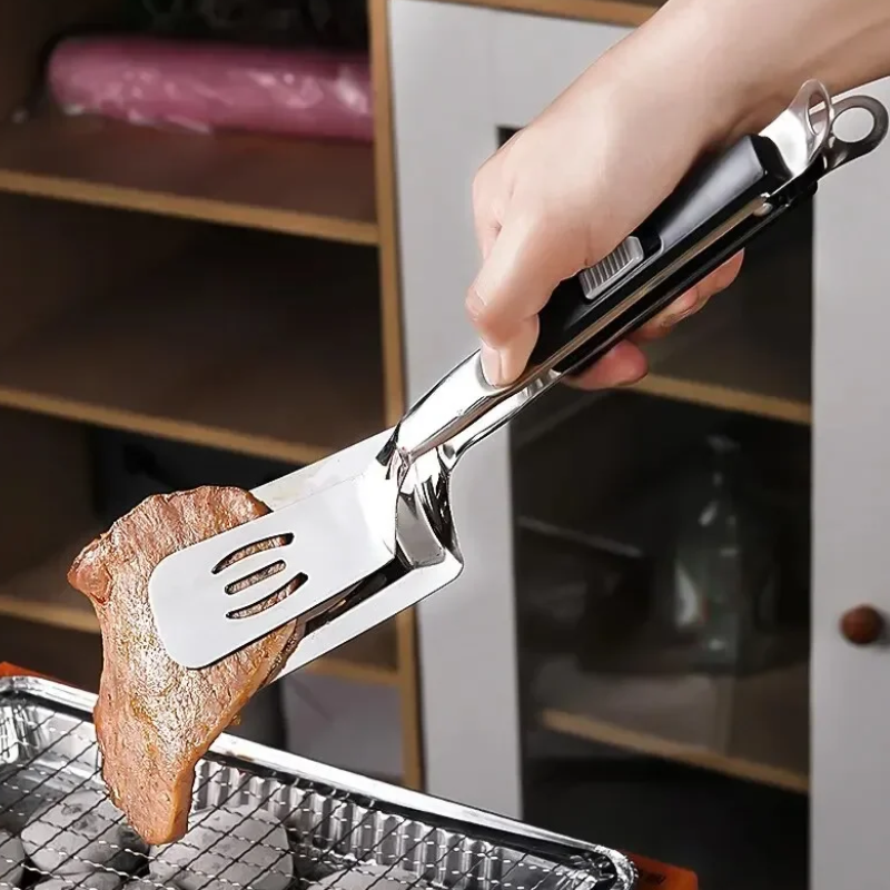 A hand uses a metal spatula tong, a versatile grilling tool, to pick up a piece of cooked meat from a grill. Shelves and cabinets are visible in the background—perfect for BBQ season cooks.