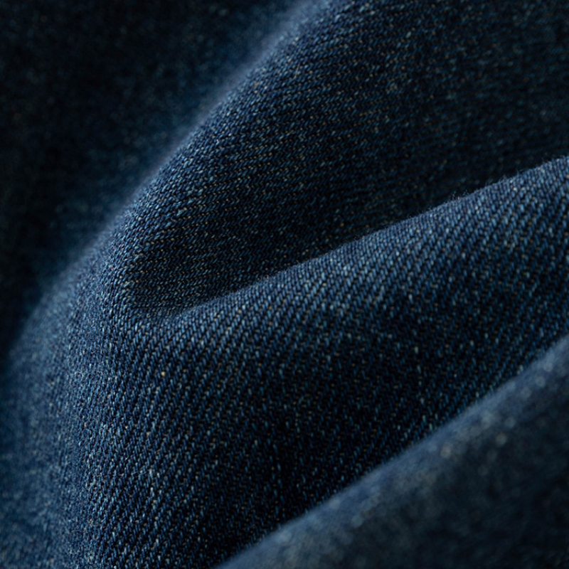 Close-up of dark blue denim fabric with visible weave texture and soft folds, showcasing shading and light—perfect for summer wear or adding a stylish edge to streetwear looks.