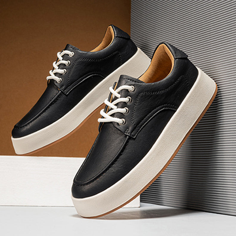 A pair of black men's leather casual shoes with white laces and thick white soles are displayed stylishly against a modern, minimalist background, offering a perfect blend of style and comfort for any occasion.