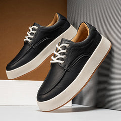 A pair of black men's leather casual shoes with white laces and thick white soles are displayed stylishly against a modern, minimalist background, offering a perfect blend of style and comfort for any occasion.
