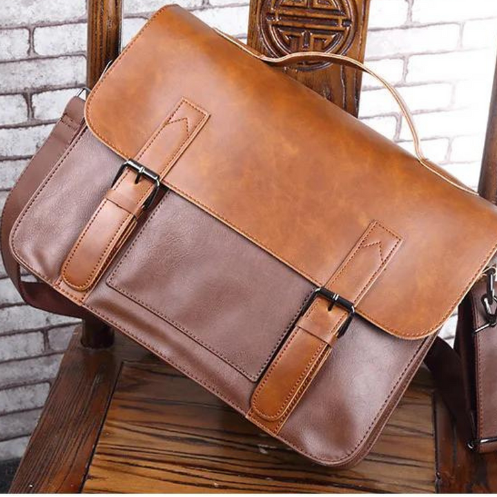 A brown premium leather satchel with buckle straps rests on a wooden chair featuring a carved circular pattern on the backrest, set against a white brick wall.