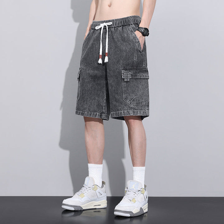 A person wearing black washed mens denim shorts with an elastic waist, white socks, white sneakers, a black watch, and a white drawstring, standing against a plain light gray background.