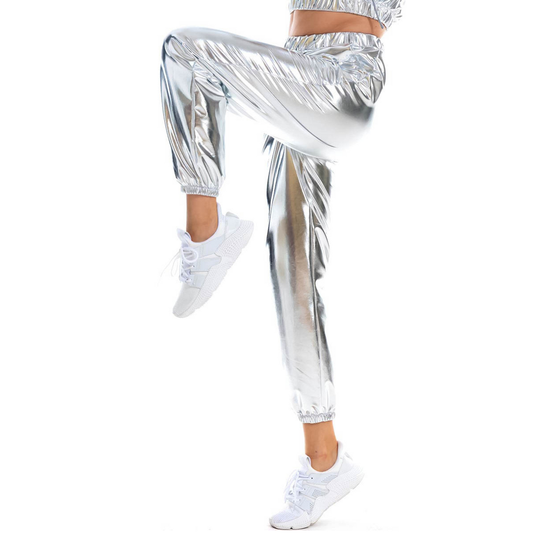 Person wearing shiny silver jogger pants with a holographic finish and white sneakers, lifting one leg as if in motion; features an elastic high waist and loose fit against a white background.