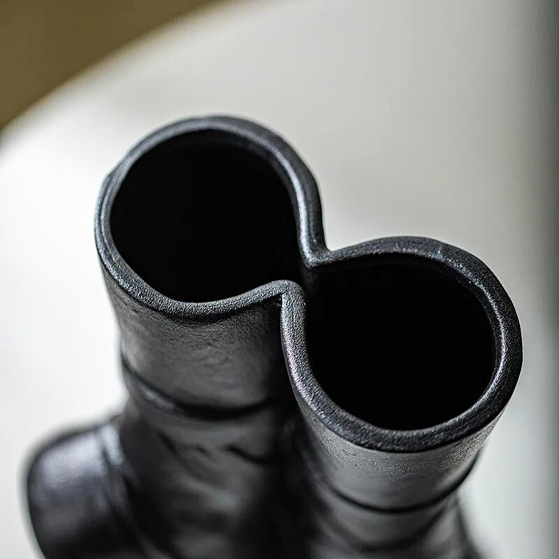A close-up view of a sculptural ceramic vase with two cylindrical openings joined together, resembling an abstract or modern art design, perfect for contemporary chic décor and placed on a light-colored surface.