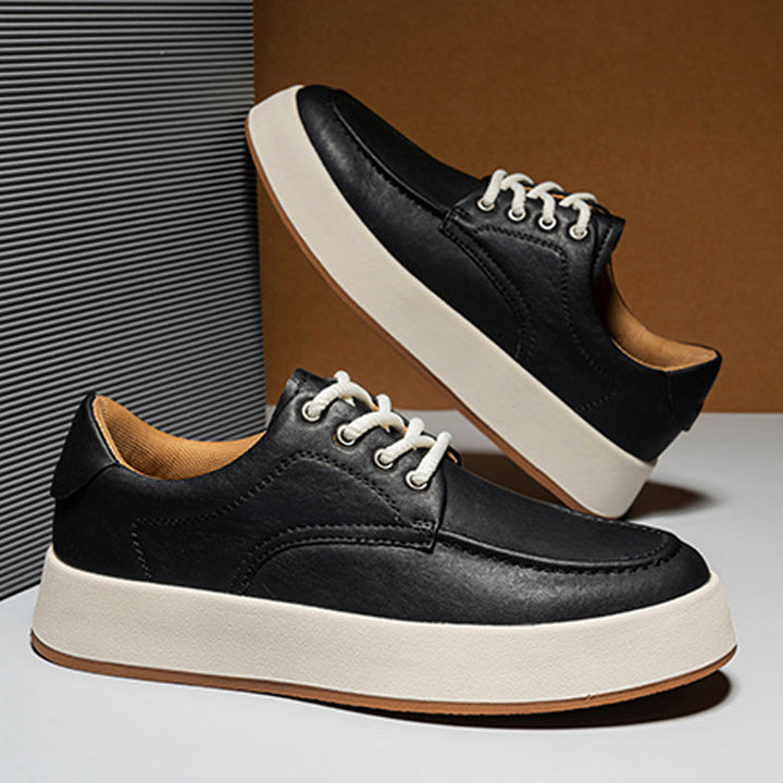 A pair of black Men's Leather Casual Shoes with white soles and laces, displayed against a geometric background—one upright, the other angled above—perfect as breathable walking shoes for everyday style.