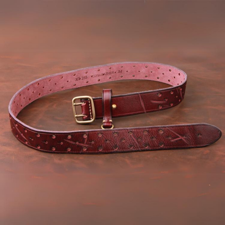 A handcrafted belt made from premium leather lies coiled on a brown surface. It features a brass buckle, small round perforations in a pattern, and visible stitching along its length.