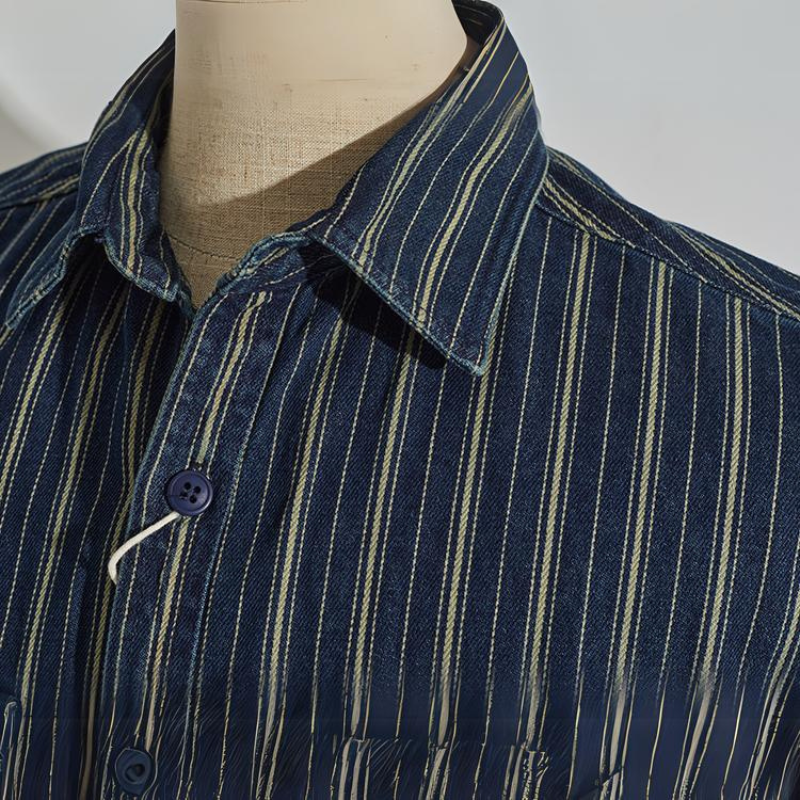 A close-up of a mannequin wearing a relaxed-fit button-down blue shirt with white and yellow vertical stripes. The focus is on the collar and top buttons of the shirt.