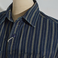 A close-up of a mannequin wearing a relaxed-fit button-down blue shirt with white and yellow vertical stripes. The focus is on the collar and top buttons of the shirt.