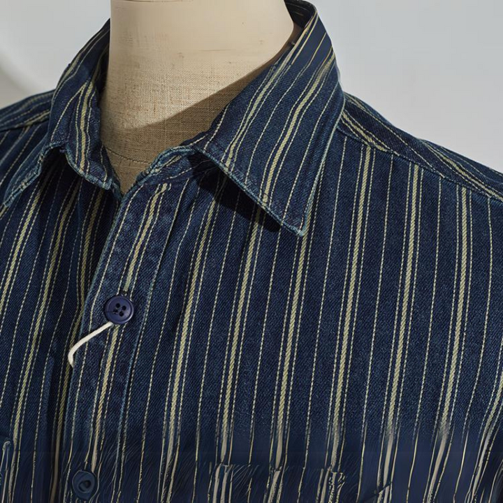 A close-up of a mannequin wearing a relaxed-fit button-down blue shirt with white and yellow vertical stripes. The focus is on the collar and top buttons of the shirt.