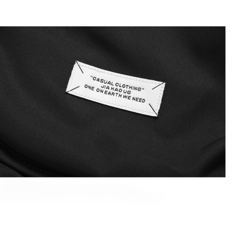 A close-up of a white fabric label sewn onto black clothing, reading: CASUAL CLOTHING JIA HAO UG ONE ON EARTH WE NEED, featured on a windproof jacket with a quilted inner lining.