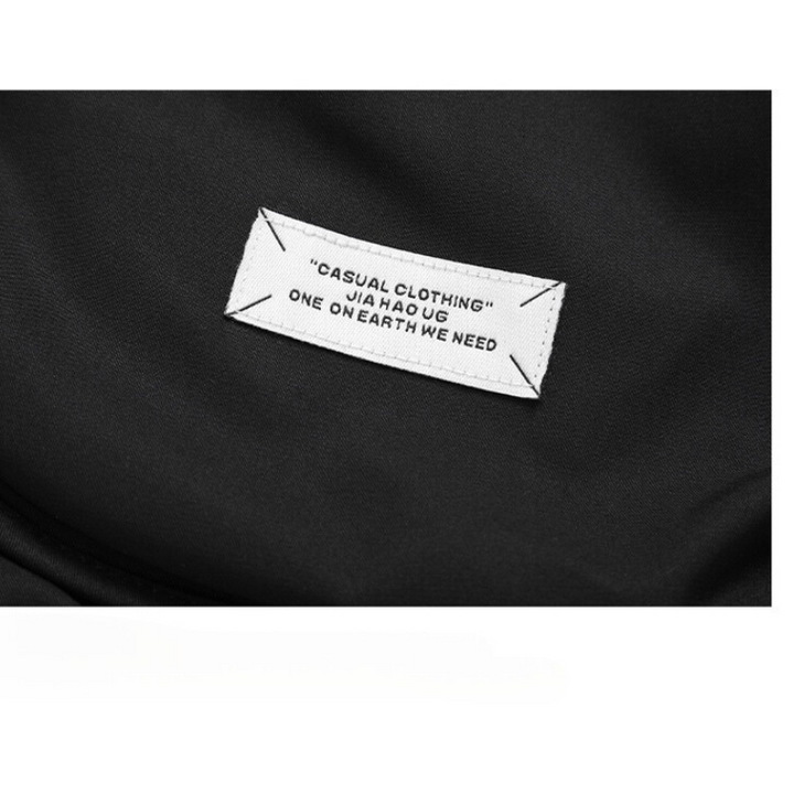 A close-up of a white fabric label sewn onto black clothing, reading: CASUAL CLOTHING JIA HAO UG ONE ON EARTH WE NEED, featured on a windproof jacket with a quilted inner lining.