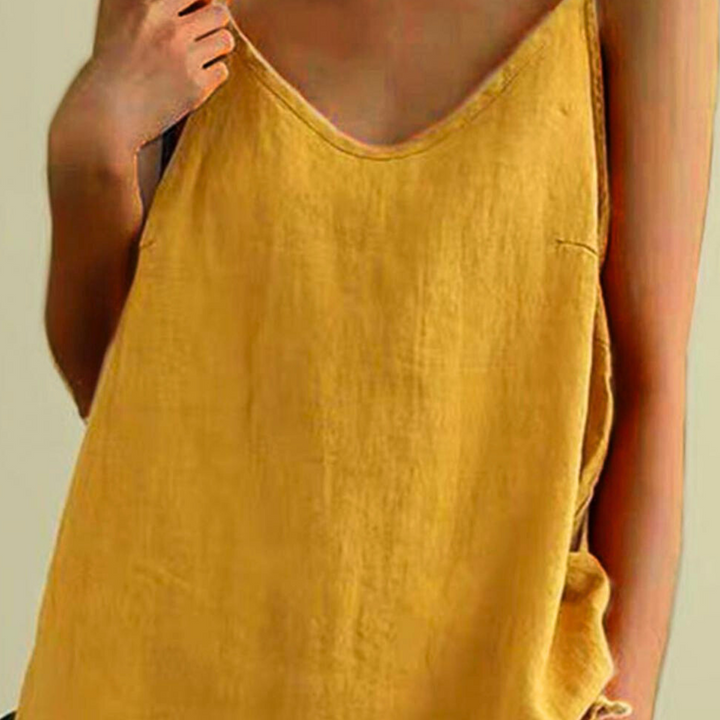A person wears a loose-fitting, sleeveless yellow top with a deep neckline and an asymmetrical hem, holding one side of the strap. The background is plain and neutral.