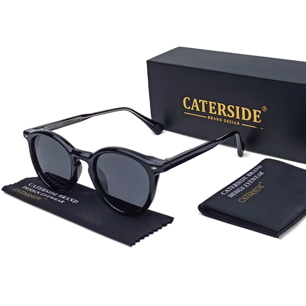 Black round frame sunglasses with dark lenses are displayed next to a black CATERSIDE box, a cleaning cloth, and a small case—all featuring the CATERSIDE brand design. Stylish and fashionable eyewear for any occasion.