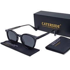 Black round frame sunglasses with dark lenses are displayed next to a black CATERSIDE box, a cleaning cloth, and a small case—all featuring the CATERSIDE brand design. Stylish and fashionable eyewear for any occasion.