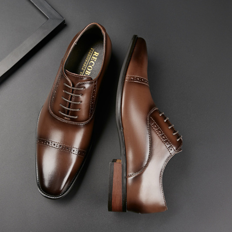 A pair of shiny brown Italian leather dress shoes with laces, featuring hand-stitched detailing and decorative broguing on the toe and sides, displayed on a dark, smooth surface.
