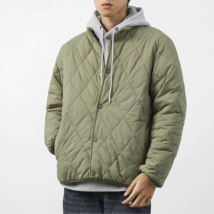 A person wearing a light green padded jacket with a diamond-stitched pattern over a gray hoodie stands against a plain white background, hands tucked into the jacket pockets.