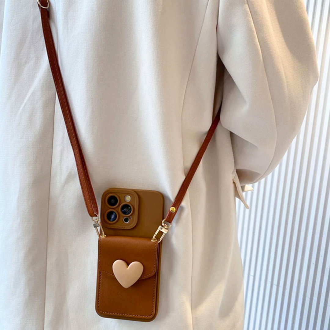 A person in a beige coat sports a chic phone case with a heart-shaped pocket, worn with a brown crossbody strap while holding a smartphone with three camera lenses. The background features vertical white lines.