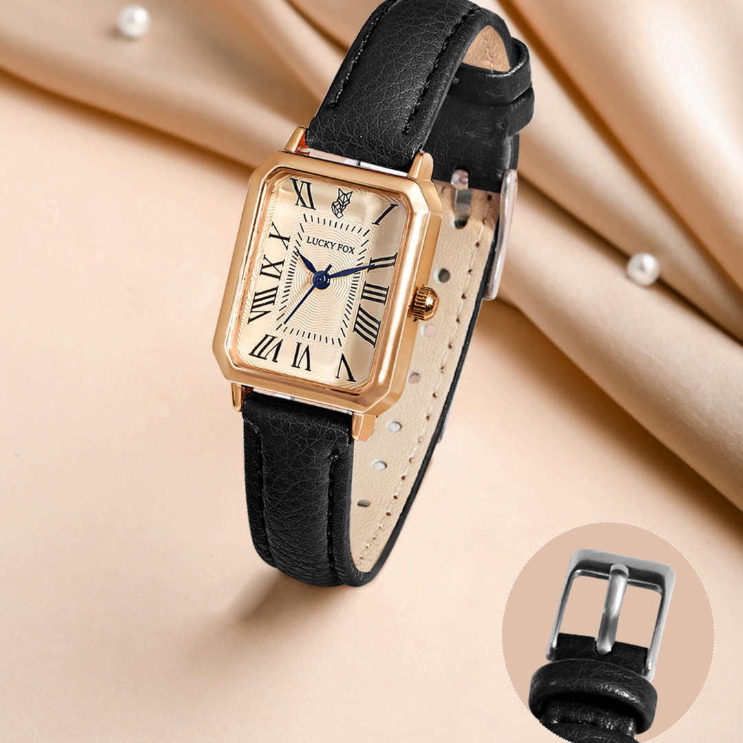 A rectangular face watch in gold with a cream dial, black Roman numerals, and blue hands. The genuine leather strap is shown in detail, highlighting its silver buckle against a beige fabric background.