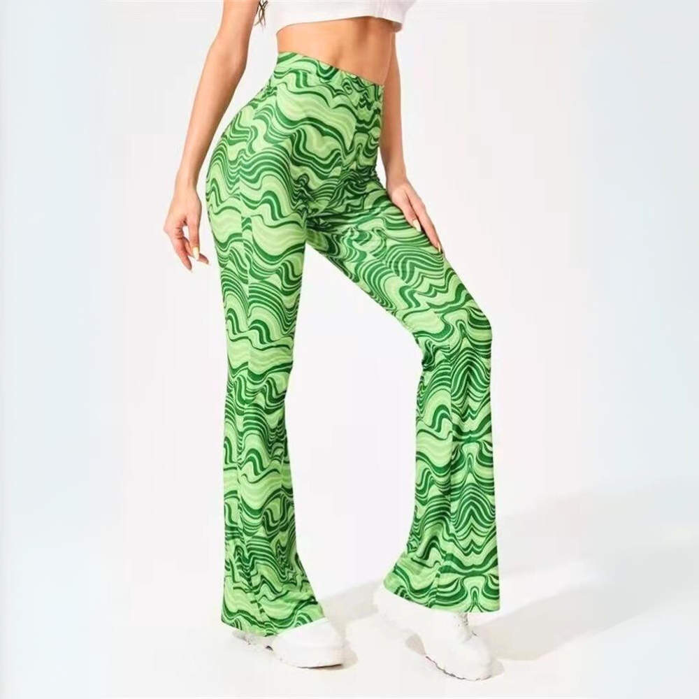 A person wearing trendy statement, green flared psychedelic flare pants with a wavy abstract pattern, a white crop top, and white sneakers, standing against a plain light background.
