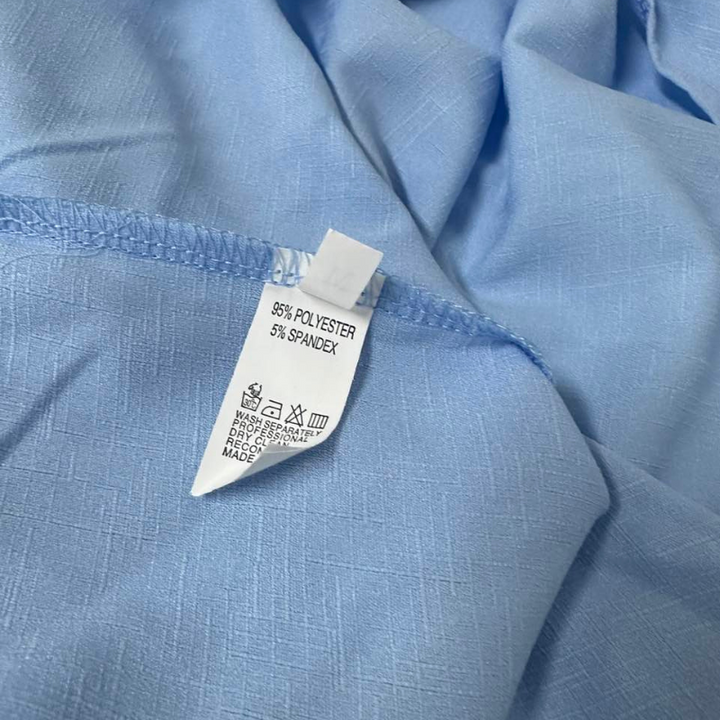 A close-up of a light blue fabric from a linen set, featuring a white care tag showing the material is 95% polyester and 5% spandex, along with washing and care symbols.