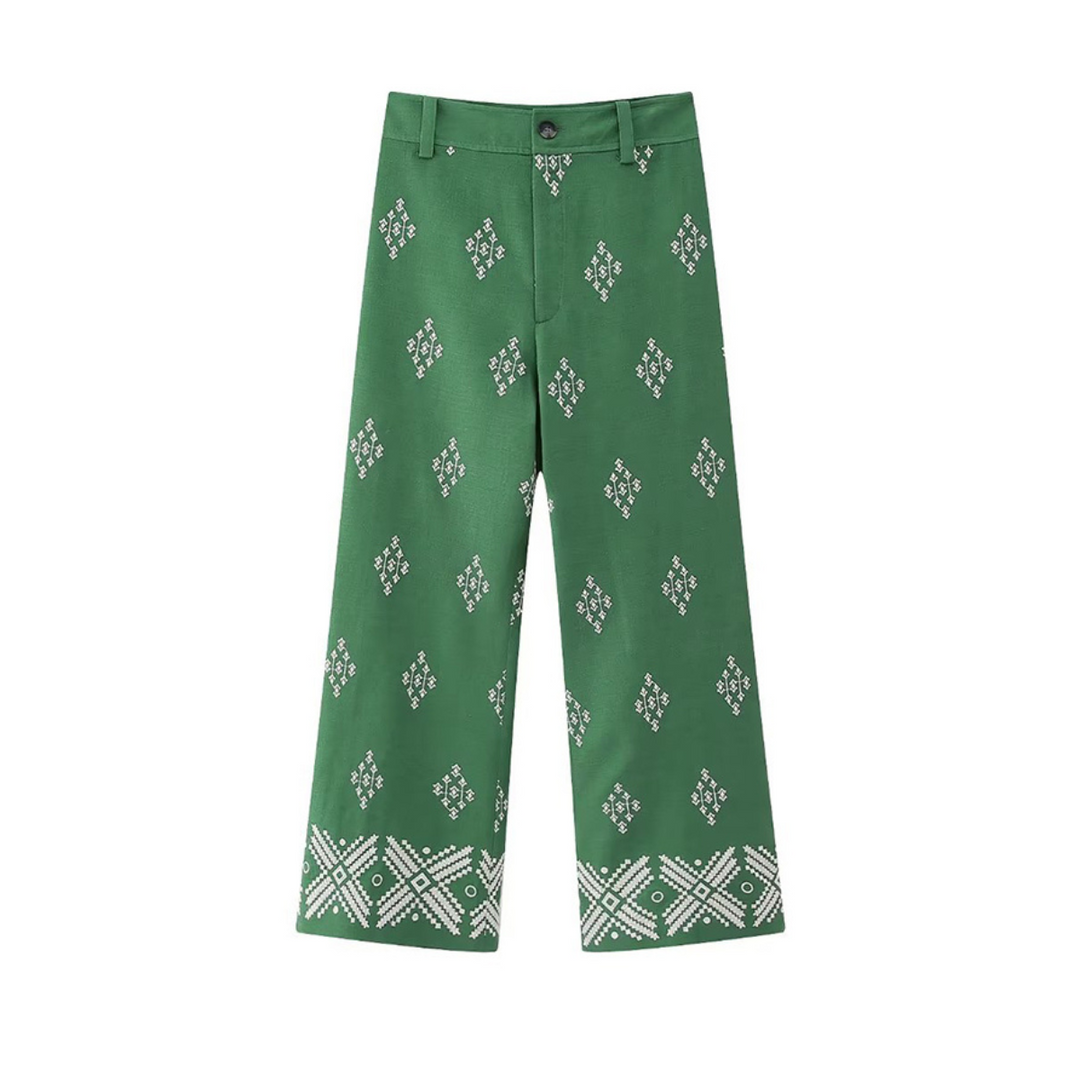 Green wide-leg trousers featuring a white diamond and geometric pattern throughout, with a more intricate design near the hem. These boho chic pants have belt loops, a button, and a zipper fly.