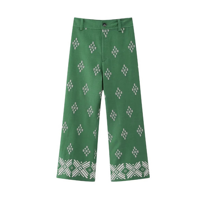 Green wide-leg trousers featuring a white diamond and geometric pattern throughout, with a more intricate design near the hem. These boho chic pants have belt loops, a button, and a zipper fly.