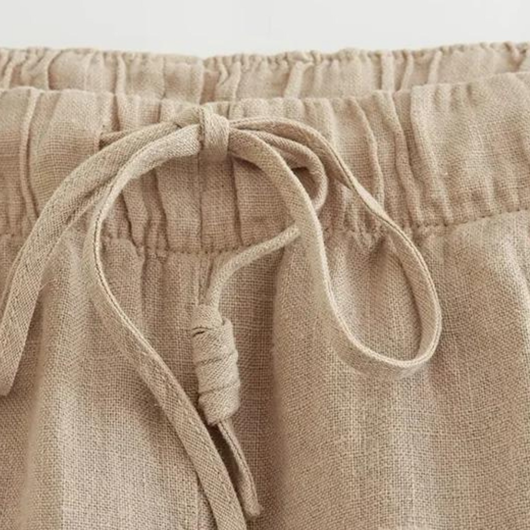 Close-up of the waistband of beige linen wide-leg pants featuring an elastic band and a tied drawstring bow at the front, perfect for effortless summer style.