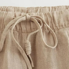 Close-up of the waistband of beige linen wide-leg pants featuring an elastic band and a tied drawstring bow at the front, perfect for effortless summer style.