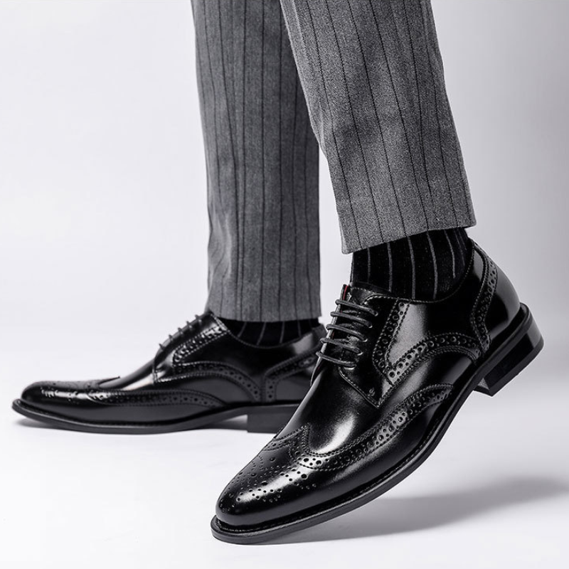 A person wearing premium leather brogue dress shoes with a cushioned insole, black socks, and grey pinstripe trousers stands on a white background.