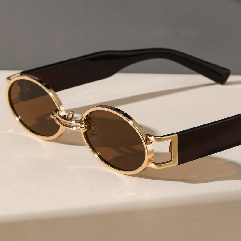 Round sunglasses with a durable metal frame, gold accents, and dark brown lenses rest on a light surface. Black arms and a unique geometric hinge design add flair, while UV400 protection ensures your eyes stay safe in bright lighting.